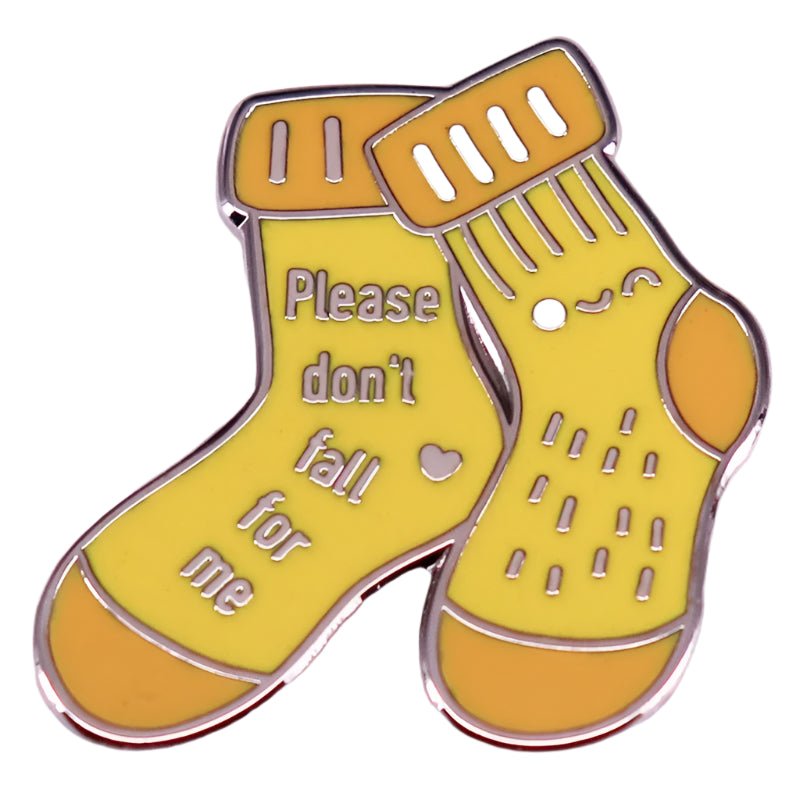My Cutesy Era enamel pin features two yellow socks—one reads Please dont fall for me with a heart, and the other shows a smiling face with playful lines.