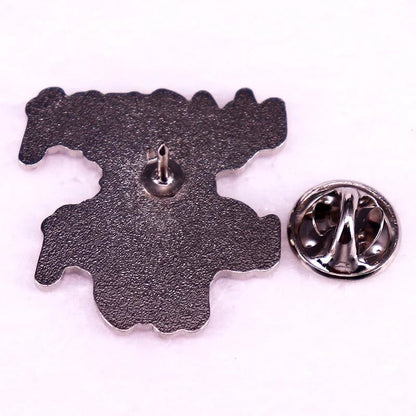 Metallic hot pink enamel pin, shaped with an irregular outline, lies face down on a light surface, displaying its pin post beside a detached round backing.