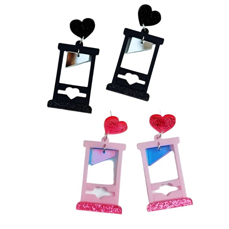 Kiss Me Later offers four pairs of acrylic heart guillotine earrings—two black with black hearts and two pink with glitter hearts—each featuring a heart-shaped top and a reflective blade.