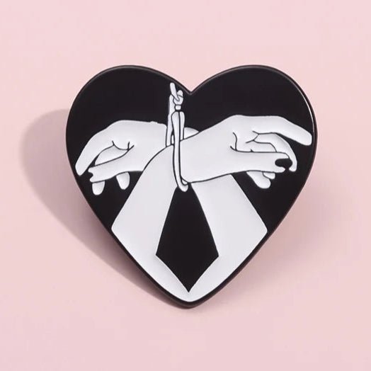 The My Cutesy Era enamel pin features two white hands bound by rope inside a heart shape, against a black background with a pink border for striking contrast.