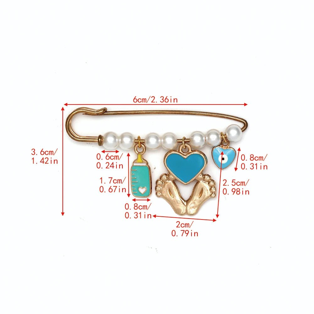 The Kiss Me Later gold safety pin, adorned with pearl beads and four charms—a blue baby bottle, heart, pacifier, and gold baby feet—makes a lovely baby shower gift. Each piece features red size labels in centimeters and inches.