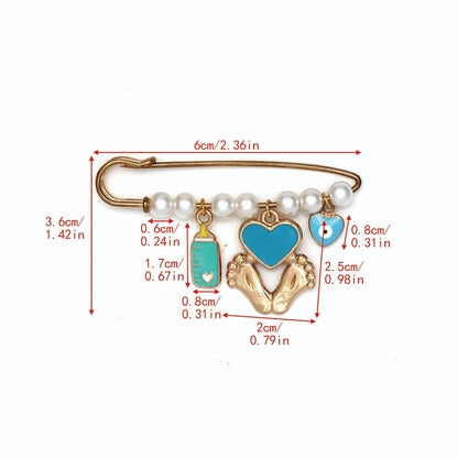 The Kiss Me Later gold safety pin, adorned with pearl beads and four charms—a blue baby bottle, heart, pacifier, and gold baby feet—makes a lovely baby shower gift. Each piece features red size labels in centimeters and inches.