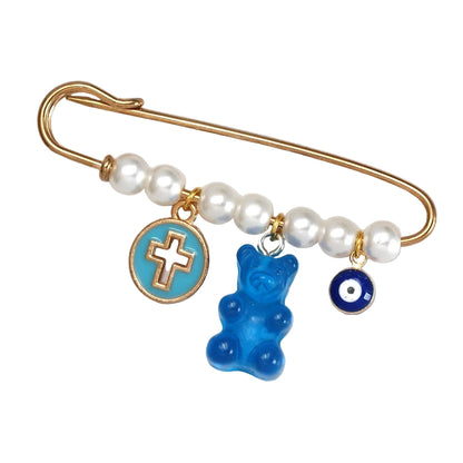From Kiss Me Later, this gold safety pin adorned with white pearls features three charms—a blue circle with a gold cross, a blue gummy bear, and a round blue evil eye—making it a stylish and unique baby shower gift.