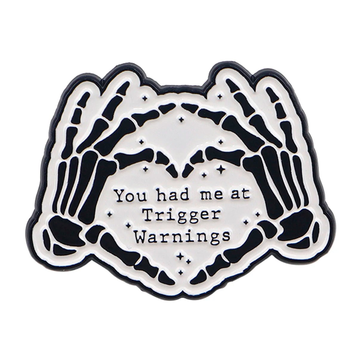 The Kiss Me Later enamel pin features two skeleton hands forming a heart around the words You had me at Trigger Warnings on a white background—perfect for adding spooky vibes to your style.