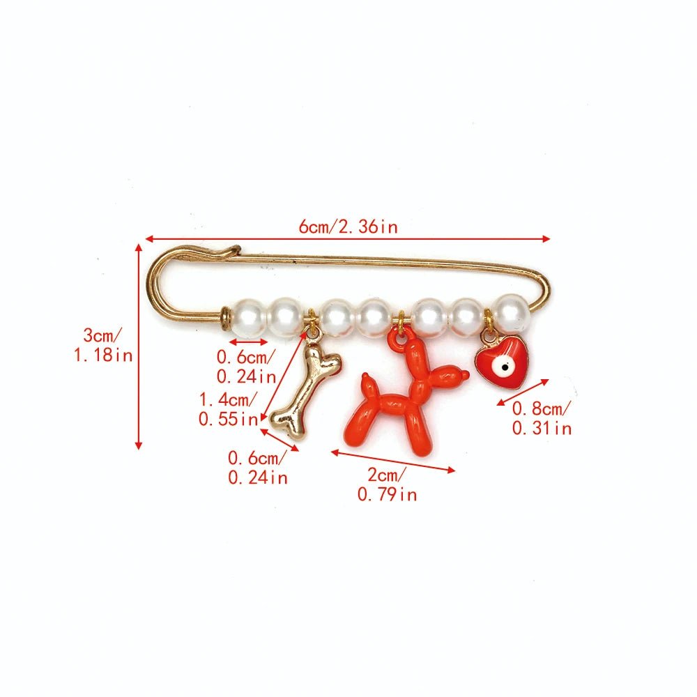 The Kiss Me Later gold safety pin brooch features beads, pearls, a bone, red balloon dog, and evil eye charms. Image displays charm and pin measurements in cm and inches. A unique baby shower gift idea.