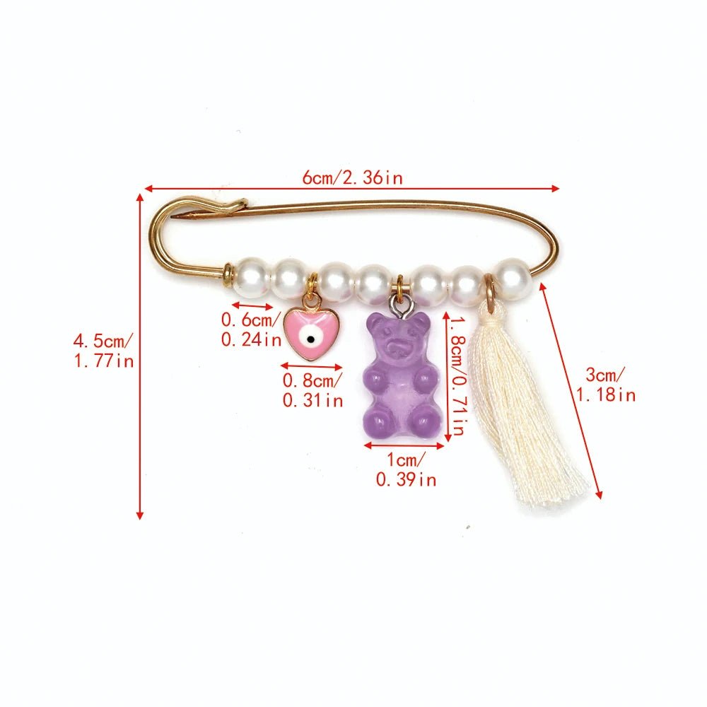 The Kiss Me Later gold brooch features pearls, a pink heart charm, a purple gummy bear charm, and a cream tassel—ideal for baby shower gifts. Sizes for each element are provided in both centimeters and inches.