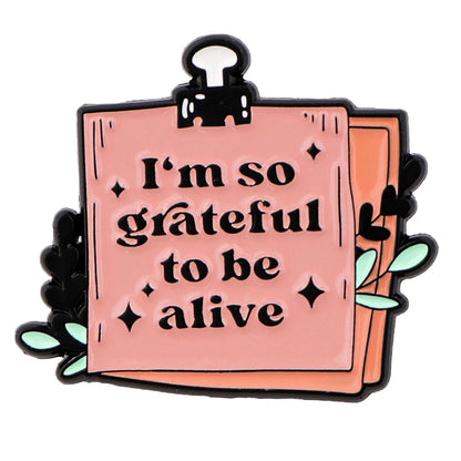 A pink Im so grateful to be alive note badge  clipped at the top with leaves and paper in the background—ideal for promoting positive affirmations and supporting mental health.