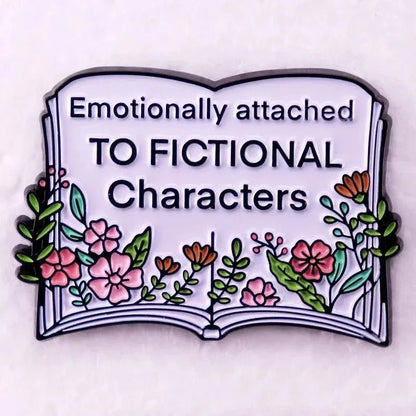 An enamel pin of an open book with flowers and the text “Emotionally attached TO FICTIONAL Characters”—perfect for romance readers or any book lover’s collection.