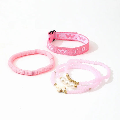 The Kiss Me Later pink bracelet stack includes a woven WWJD bracelet, a solid pink disc bracelet, and two beaded bracelets with gold and white beads, all displayed on a white background.