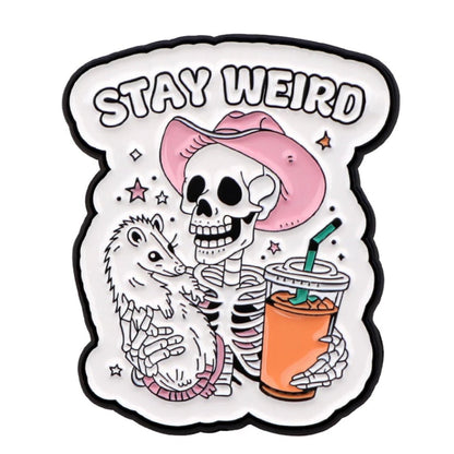 A cartoon skeleton in a pink cowboy hat holds a possum and an orange drink under bold STAY WEIRD text. The white background features small stars. Brand: Kiss Me Later.