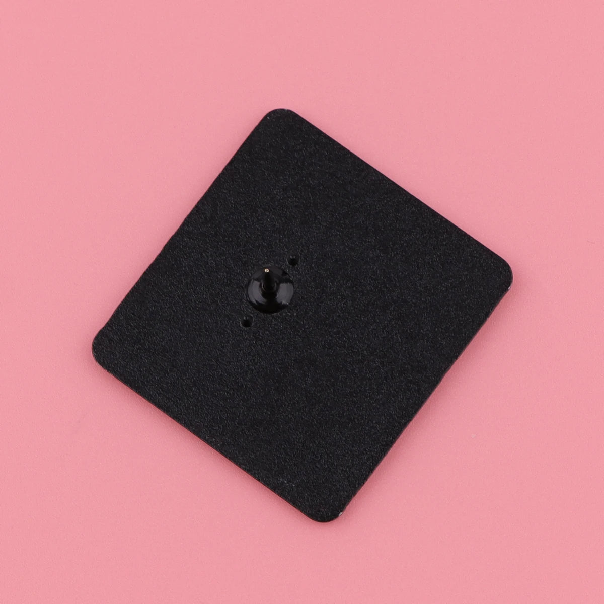 A black, square Kiss Me Later clock movement mechanism with a central spindle sits on a pink background, surrounded by subtle spooky vibes.