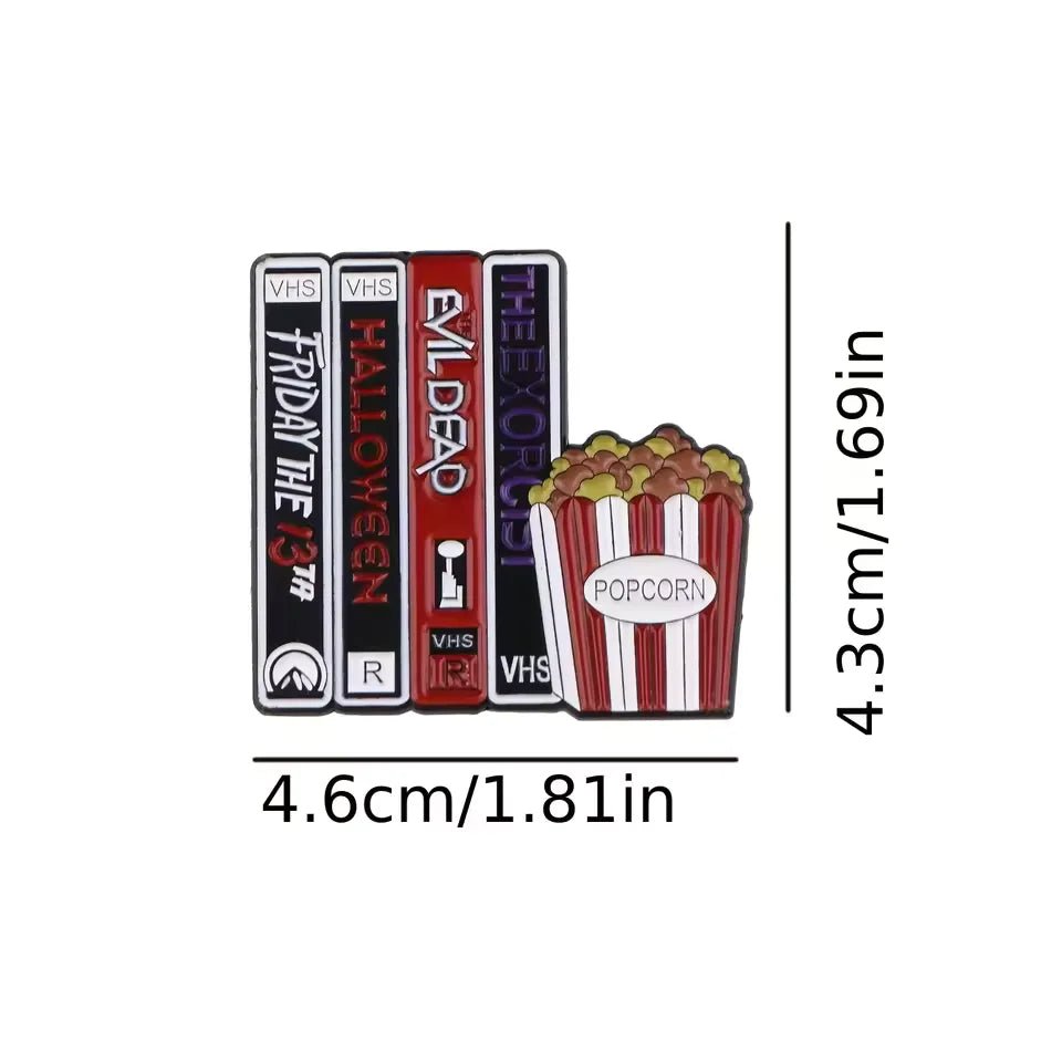The Kiss Me Later enamel pin features three VHS tapes labeled Friday the 13th, Halloween, Evil Dead, and The Exorcist next to a popcorn bucket. Ideal for movie buffs and collectors. Size: 4.6 x 4.3 cm.