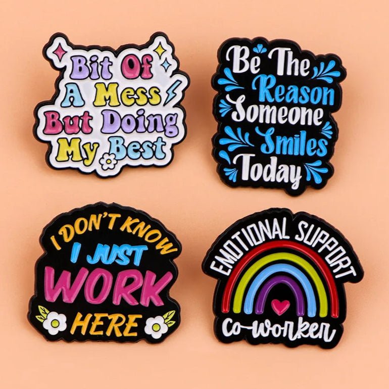 Four colorful  pins on a peach background feature playful messages in fun fonts—perfect as a coworker gift or cheerful motivational or emotional support enamel pins to brighten anyone’s day.