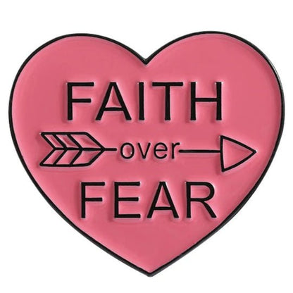 Show your Faith Over Fear with this red pink heart-shaped enamel pin featuring a black FAITH Over FEAR design and an arrow pointing right through over.