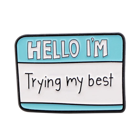 A Kiss Me Later name badge with a blue top that says HELLO IM and a white bottom reading Trying my best in handwritten style, just like the Hello Im Trying My Best enamel pin.