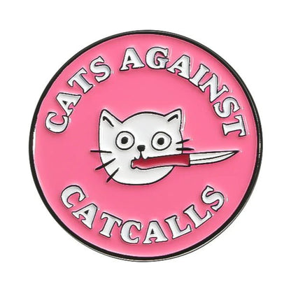 My Cutesy Era’s pink, circular “Cats Against Catcalls” enamel badge features a white cat face with a knife in its mouth and bold lettering around the edge.