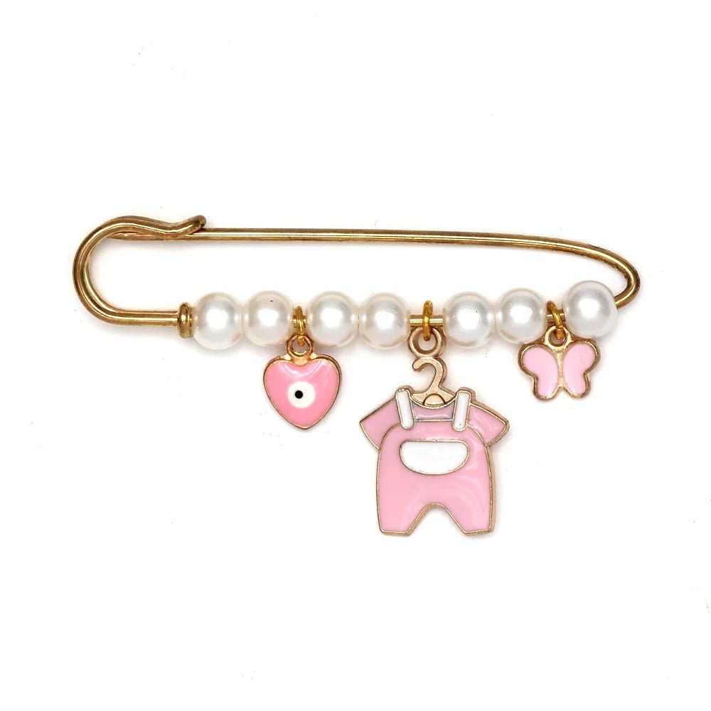 The Kiss Me Later gold safety pin features white pearls and beads, holding three pink charms—a heart, baby romper, and butterfly—making it a charming baby shower gift or unique brooch.