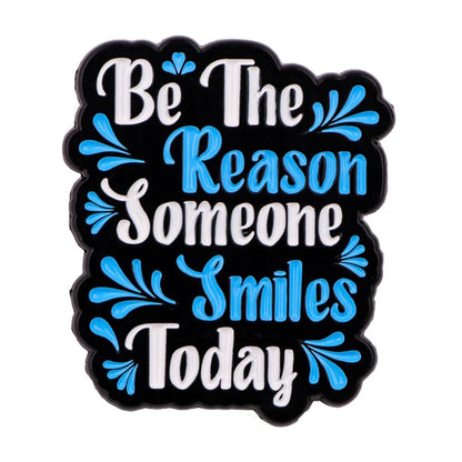 Black sign with white and blue text reads: Be the reason someone smiles today. A thoughtful coworker gift or pair it with a motivational enamel pin for daily inspiration.