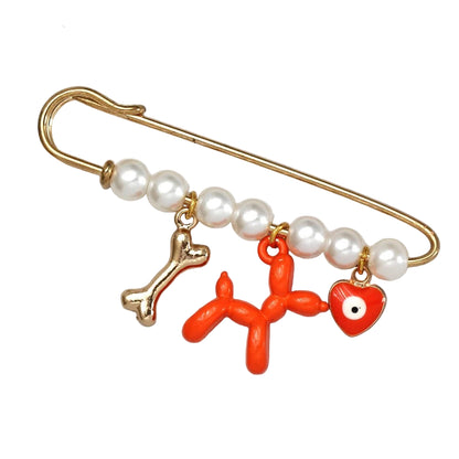 Kiss Me Later’s gold evil eye pin features five white beads and three dangling charms—a gold bone, orange balloon dog, and red heart with an eye—making it a unique baby shower gift.