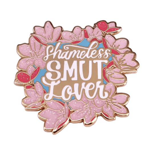 Add flair to your collection with an enamel pin—pink flowers and bold “Shameless SMUT Lover” in white and beige on blue—a playful must-have for every book lover!.