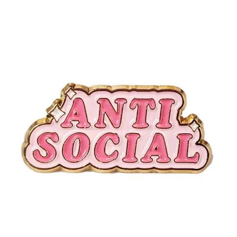 A gold-trimmed enamel pin by Kiss Me Later featuring ANTI SOCIAL in bold pink letters on a light pink background—a unique mental health accessory for self-expression.