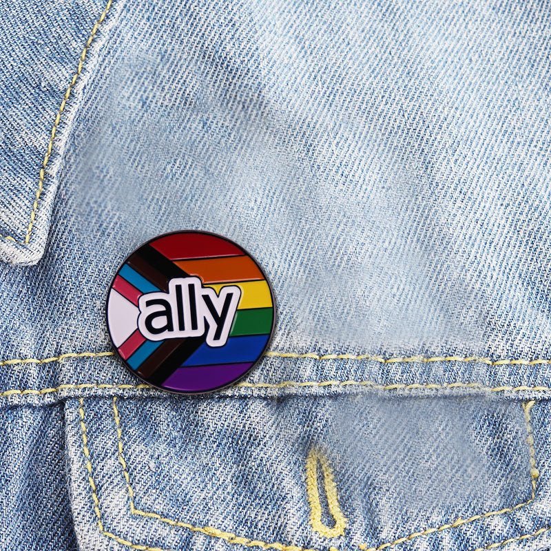 Pride flag ound enamel pin features ally on a rainbow and progress pride flag, shown on a light blue denim jacket. Ships worldwide.