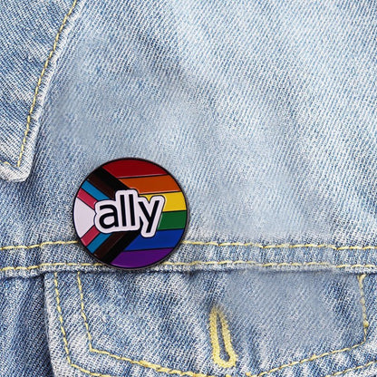 Pride flag ound enamel pin features ally on a rainbow and progress pride flag, shown on a light blue denim jacket. Ships worldwide.
