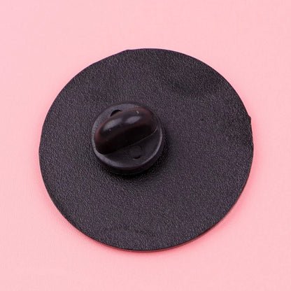 A black round enamel pin with a butterfly clutch features Being Kind Is Punk and rests on a pink surface—an ideal pride accessory to express your values.