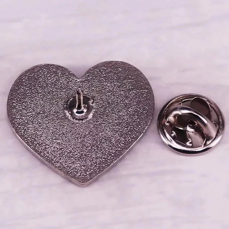 A silver heart-shaped pin with a textured surface is displayed face down beside its round butterfly clutch, both on a light background—an elegant accessory. Enjoy worldwide shipping.