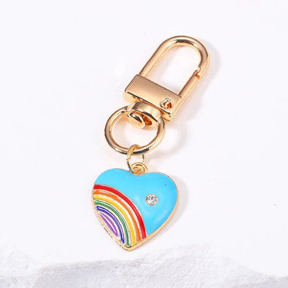 Blue and rainbow flag keychain features a gold finish and a blue heart-shaped rainbow charm with a gemstone—perfect as a pride accessory for your bag or keys.