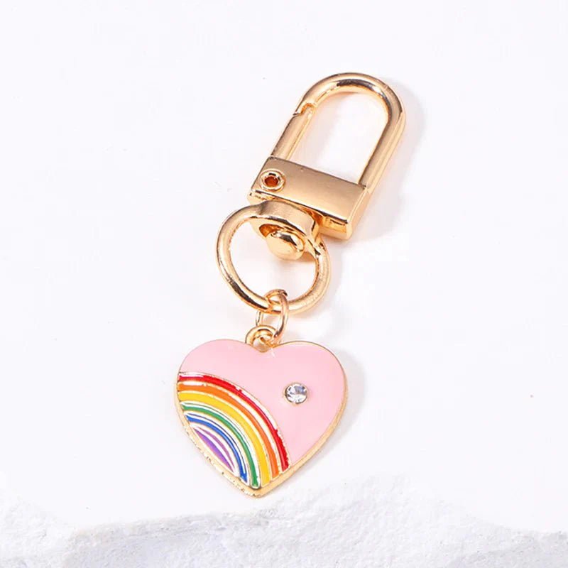 Rainbow pride chain features a gold ring and a pink heart-shaped charm with a small gem and colorful rainbow design, displayed on a white surface.