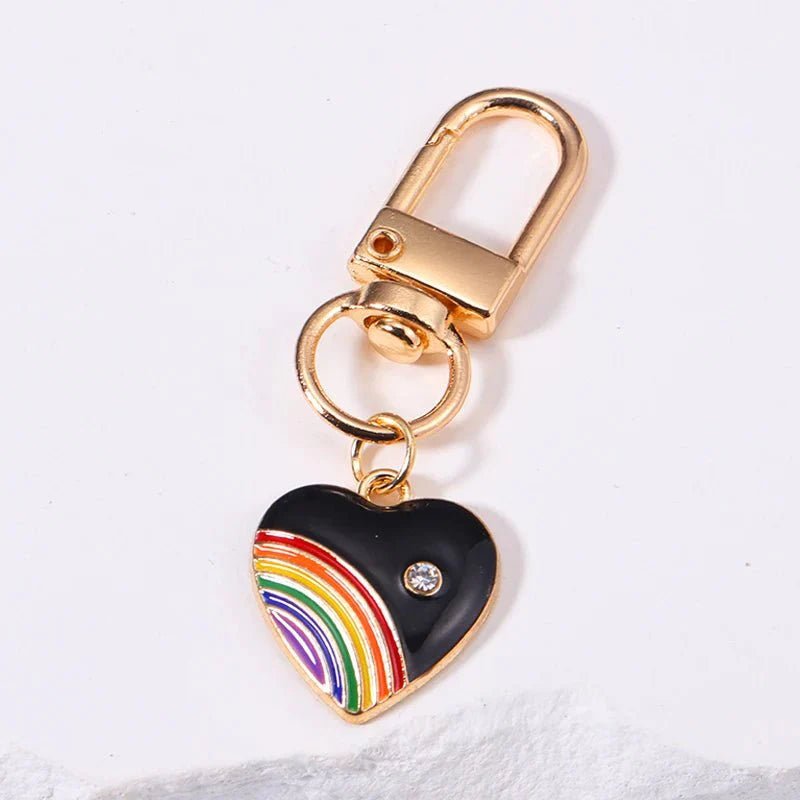 Rainbow pride chain features a gold keyring and black heart-shaped rainbow charm with a rhinestone accent, displayed on a white surface—perfect as a pride accessory.