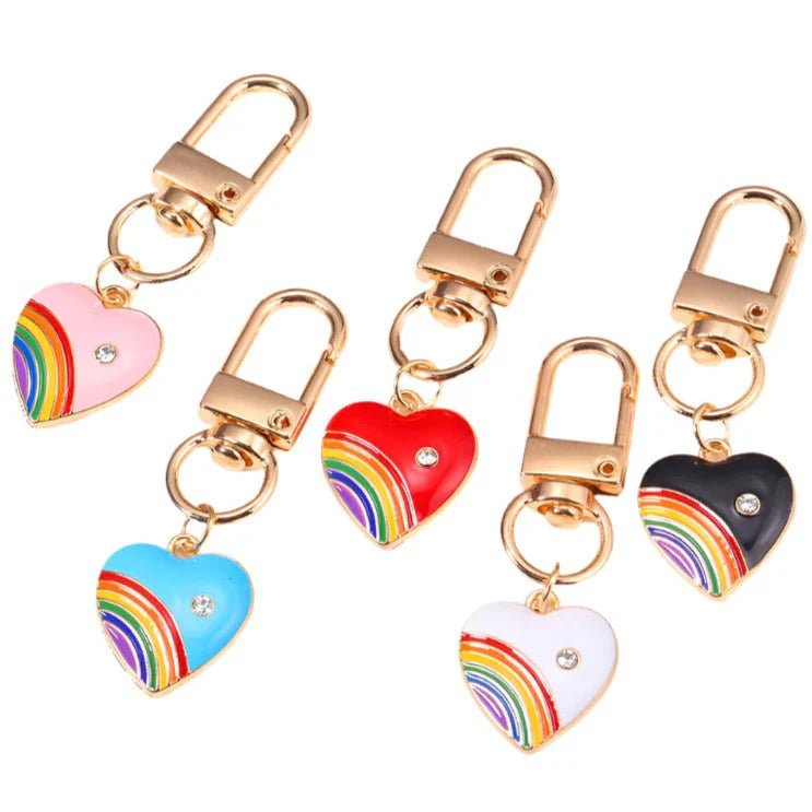 Five gold keychains with heart-shaped rainbow charms and rhinestones, available in pink, blue, red, white, and black—a vibrant pride accessory for use as a colorful bag charm or rainbow keychain.