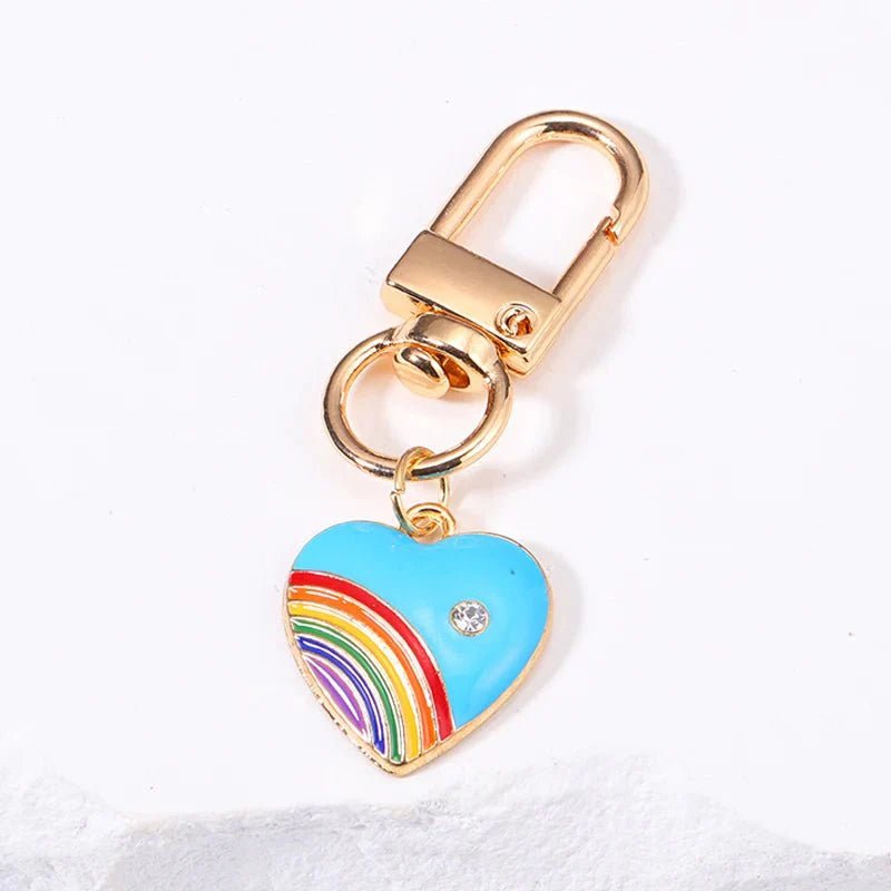 Pride rainbow heart key chain with a gold keyring, blue heart-shaped rainbow charm, and clear gem on a white background—perfect as a pride accessory.