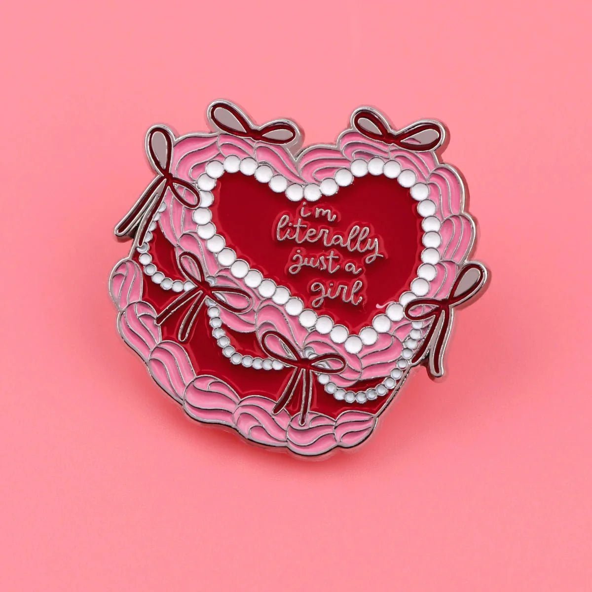 A dreamy heart-shaped enamel badge with pink ruffles, bows, and pearls on a pink background. Features Im Literally Just a Girl in white cursive—perfect for fans of pink and red cake badge designs.