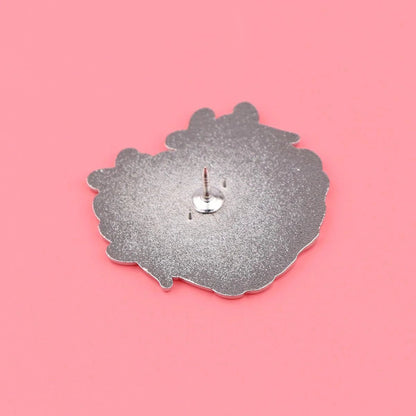 metallic enamel badge with an irregular shape is face down on a pink background, revealing its sharp post and backing attachment.