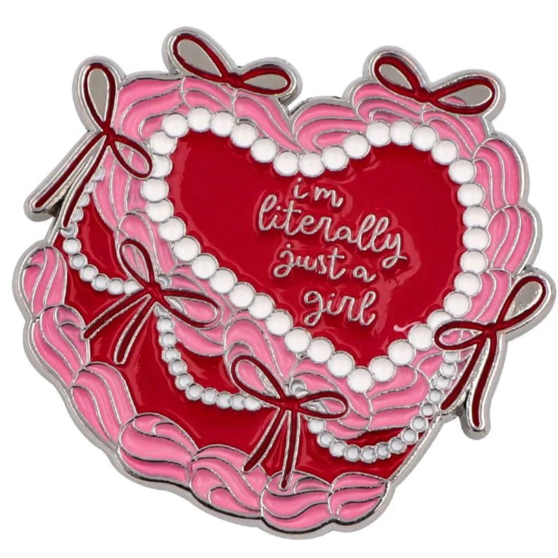 A heart-shaped enamel badge featuring pink and red ribbons, white pearl accents, and Im Literally Just a Girl in cursive—ideal as a cute pink and red cake accessory.