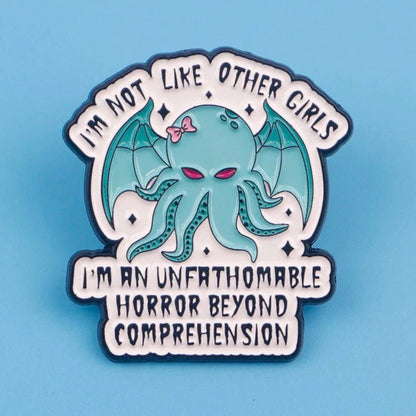 The Kiss Me Later enamel badge features a cute, cartoon Cthulhu with a pink bow and bat wings, surrounded by the text: I’m not like other girls. I’m an unfathomable horror beyond comprehension, on a light blue background.