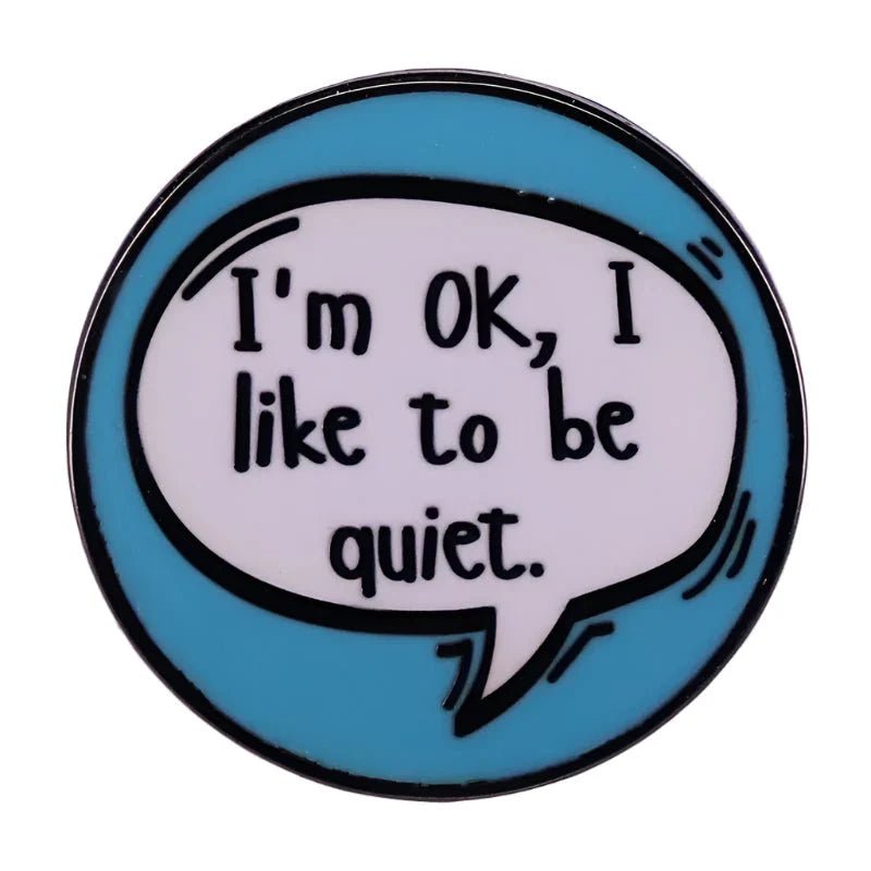 A round Gay Skate Introvert Enamel Pin with a blue border and a white speech bubble that says I’m OK, I like to be quiet. in black handwritten-style text—a subtle pride accessory for those who value quiet moments.
