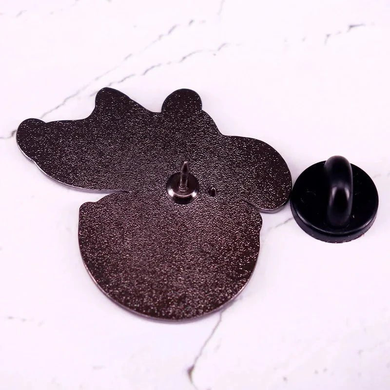 A kawaii queer enamel pin by Gay Skate, shaped like an animal and shown from the back with its black rubber pin backing removed, is displayed on a white marble surface.