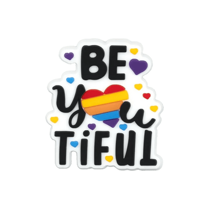 Kiss Me Later sticker featuring “BE YOU TIFUL”—the word “YOU” is styled with a rainbow heart, plus pride-themed charms and hearts, including Trans Flag accents, on a white background.