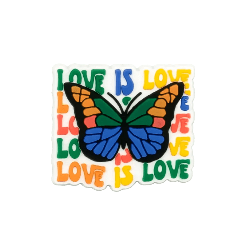 A vibrant Kiss Me Later charm features a colorful butterfly with green, orange, and blue wings atop a white square that repeats “LOVE IS LOVE” in rainbow colors—a perfect celebration piece for pride.