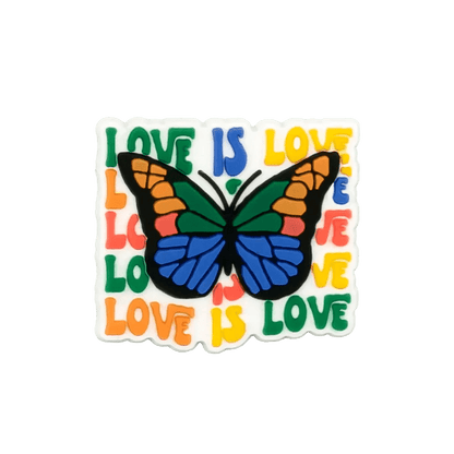 A colorful butterfly with orange, blue, green, and black wings features over a LOVE IS LOVE pride flag text background, accented by subtle pride charms on a white square. Brand: Kiss Me Later.