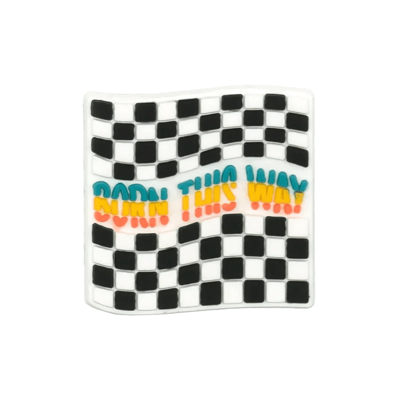 A wavy black-and-white checkered flag by Kiss Me Later, featuring BORN THIS WAY in blue, yellow, and red across the center, accented with pride-themed charms.