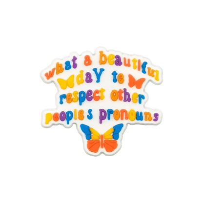 Kiss Me Later’s colorful text reads, What a beautiful day to respect other peoples pronouns, accented by butterflies and pride charms on a transparent background.