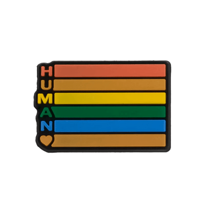 A rectangular Kiss Me Later pin, inspired by the Rainbow Flag, has five horizontal stripes (red, orange, yellow, green, blue) with HUMAN in black vertically on the left and a heart at the bottom—perfect for pride charms.