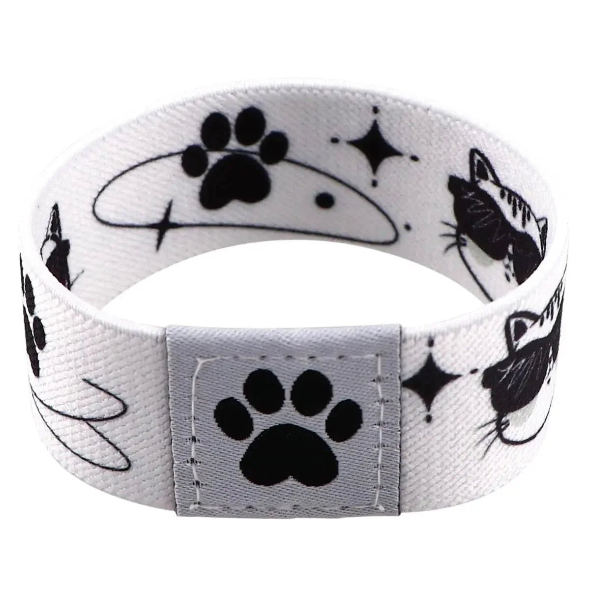 The Gay Skate white fabric wristband features black cat faces, paw prints, stars, and swirls with a stitched paw patch, shown in a circular shape—a charming Pride accessory for any occasion.