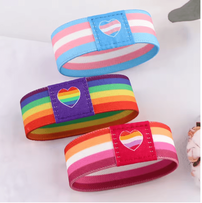 Gay Skates set of three fabric wristbands features a light blue and pastel lesbian pride heart band, a rainbow-striped band with heart, and a pink band with another lesbian pride heart—perfect colorful accessories for Pride.