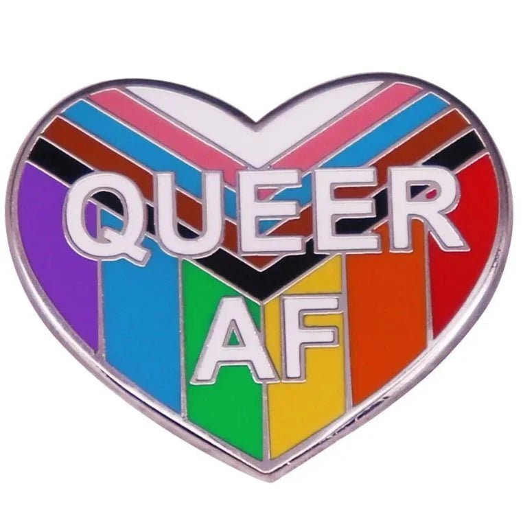 heart-shaped pin with QUEER AF text on a bright rainbow background, featuring bold Progress Pride Flag colors—black, brown, light blue, pink, and white stripes.