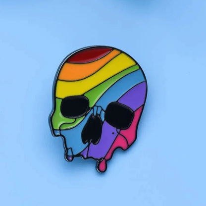 Rainbow pride skull enamel pin features hollow eyes and nose, melting rainbow stripes, and a light blue background. Ships worldwide.